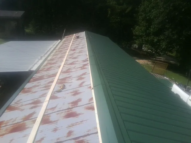 Old rusted panels beside newly installed green metal roofing — Wind Damage Roof Repair by Roofing Brothers in Brainard