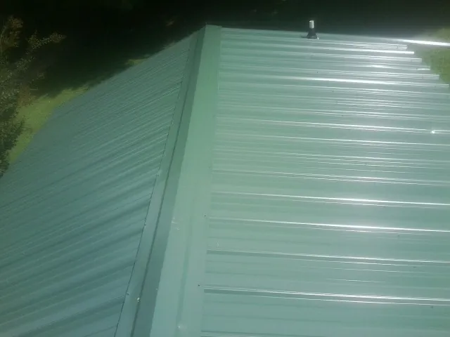 New green metal panels meeting at the ridge of a roof — Flat Roof Repair work by our crew in Brainard