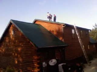 Crew on the ridge of a green metal roof on a two story log home in Brainard