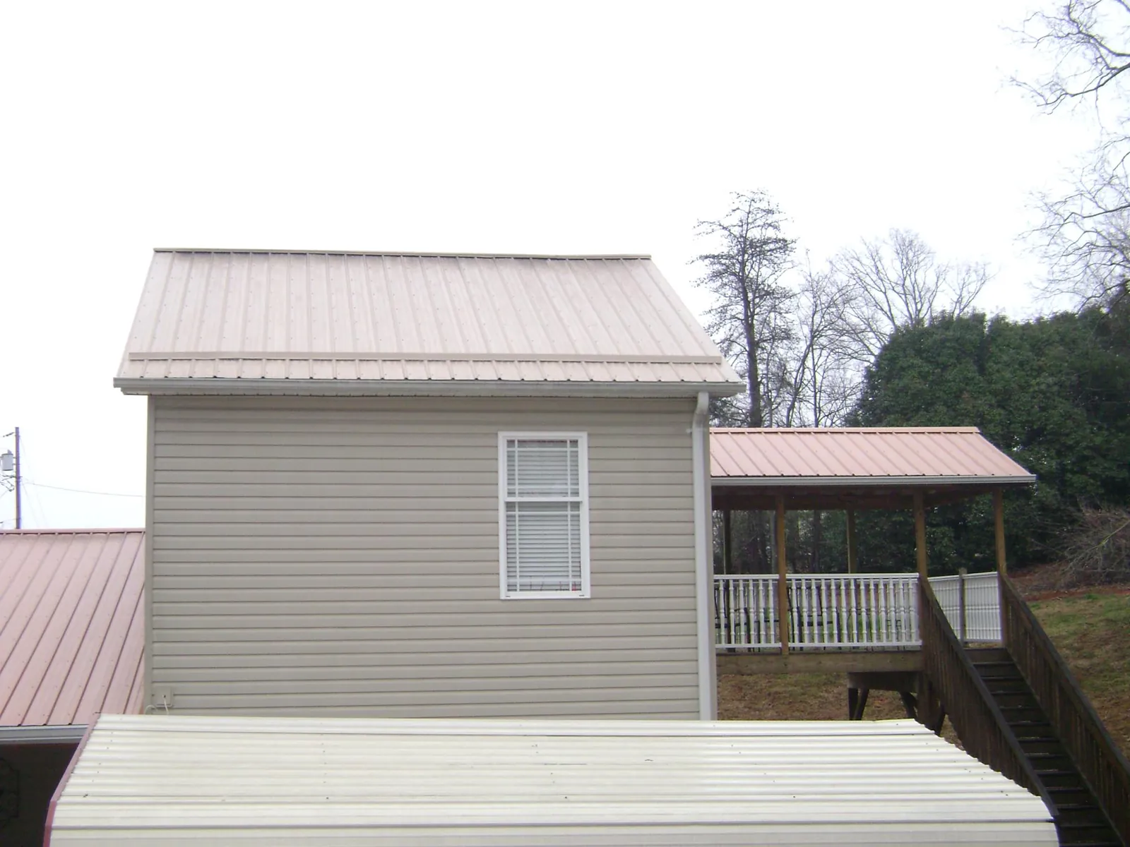 Tan metal roofs on a two story addition and attached porch, from a Roof Replacement job in Brainard